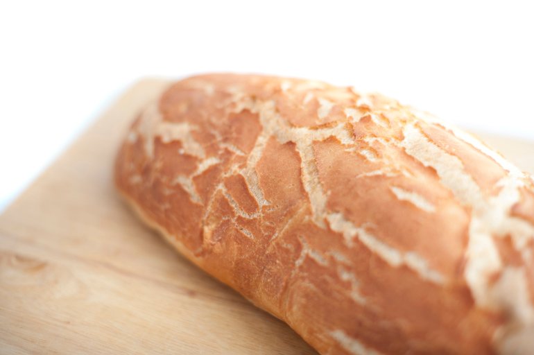 Close up view with shallow dof of a freshly baked crusty loaf of white bread on a wooden bread board over white