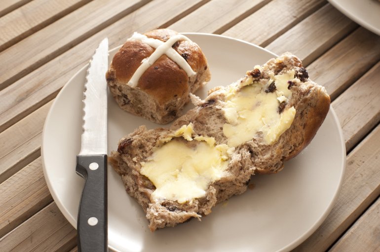 Photo of bread with butter, bun and knife on plate on wooden table. Daylight