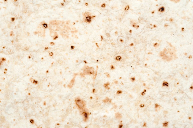 Background texture of a the surface of a baked tortilla, a thin disk of bread made with unleavened flour