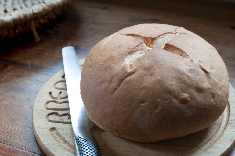Round crusty cob roll on a wooden bread board with a bread knife, close up high angle view