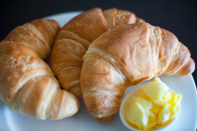Freshly baked flaky crescent shaped croissants served for breakfast with curled butter in a side dish