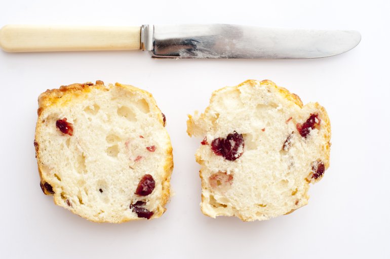 View from above of the two halves of a cut freshly baked homemade fruity scone with a bone handled knife above on a white background
