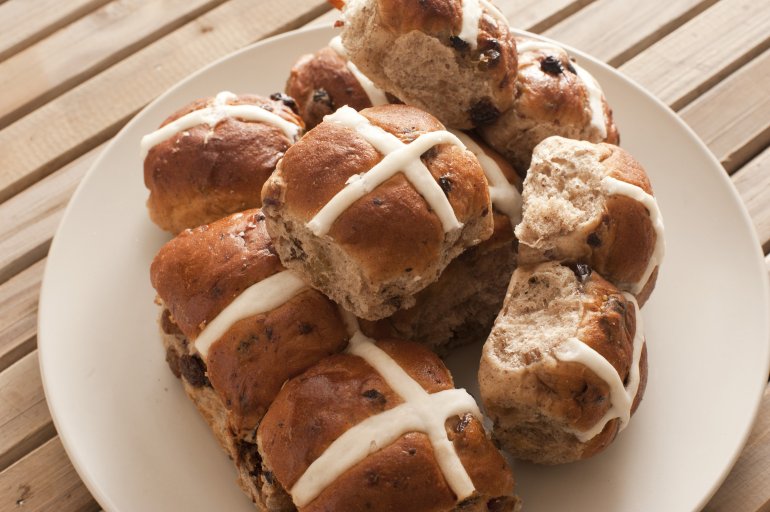 Batch of delicious spicy hot cross buns with raisins served on a plate for an Easter snack symbolising the crucifixion of Christ