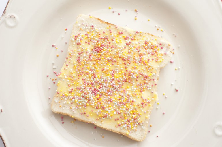 Buttered slice of white fairy bread covered in colorful sprinkles for a childhood treat for kids, overhead view on a white plate