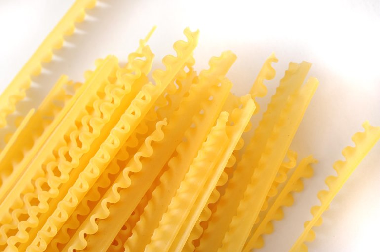 Dried reginette pasta with its distinctive frilly wavy edges for use in traditional Italian cuisine, overhead view on white