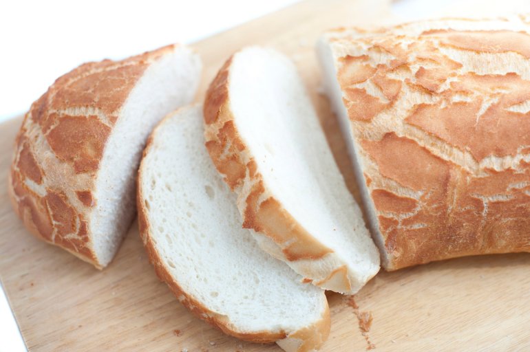 Sliced fresh white crusty bread loaf on a wooden bread board over a white background