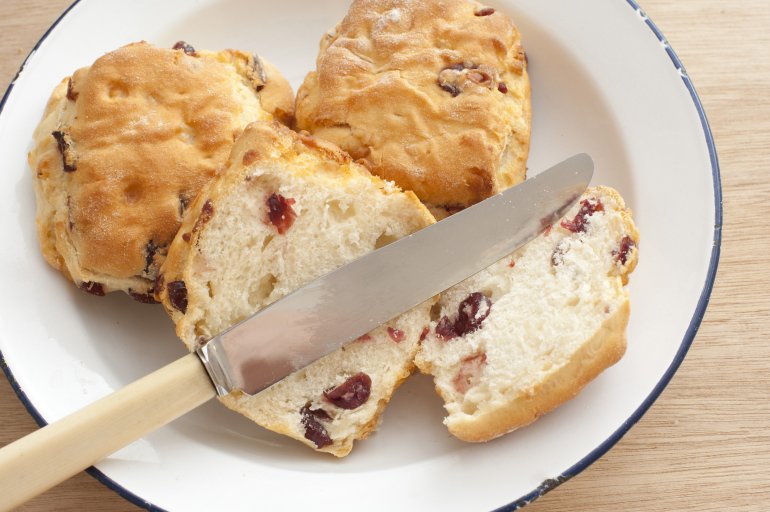 Sliced freshly baked scone with fruity raisins and a bone handled knife viewed from overhead on a white plate