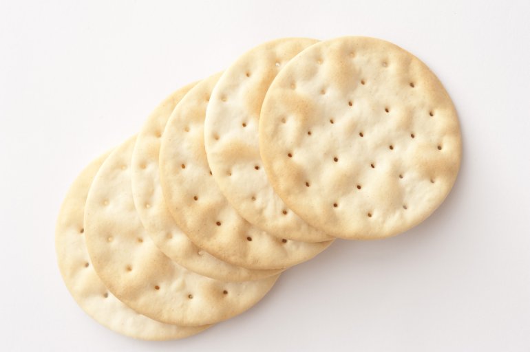 Row of plain crispy water crackers to accompany a cheese platter arranged diagonally on a white background with copyspace, overhead view