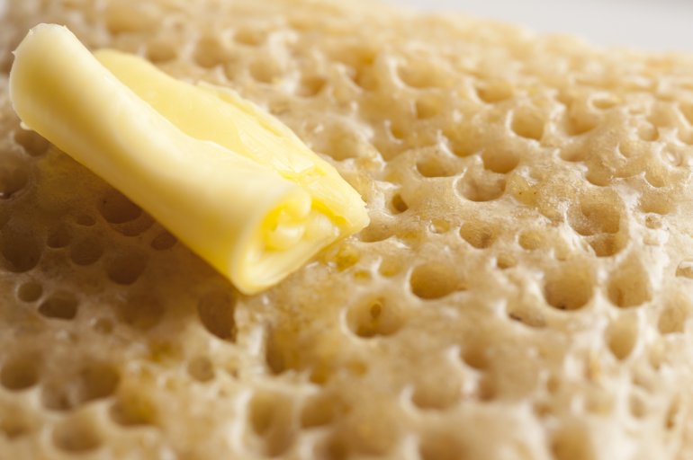 Melting curved slice of yellow butter on top of delicious hot crumpet, bread or pancake