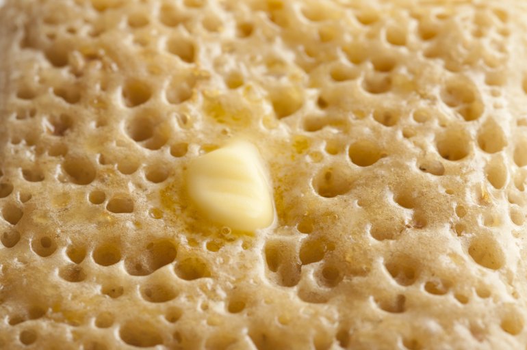 Extreme close up of one golden porous crumpet with melting triangle of butter