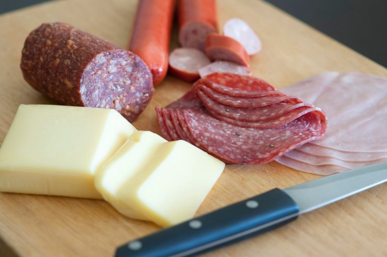 Wholesome traditional German breakfast on a chopping board with sliced cheese, salami, sausage and cold meats alongside a kitchen knife used in the preparation