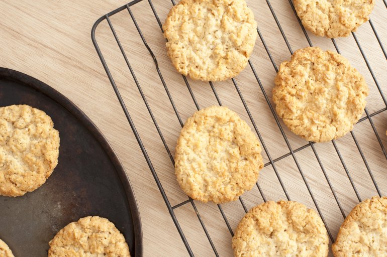 Delicious home baked crispy oat cookies cooling on a wire rack on a wooden kitchen counter, overhead view