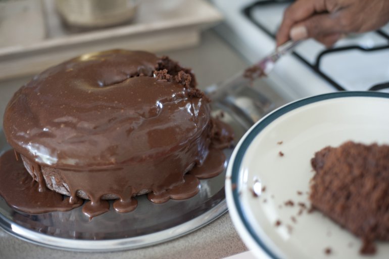 Freshly baked homemade chocolate mud cake with dripping icing being cut and served on a plate