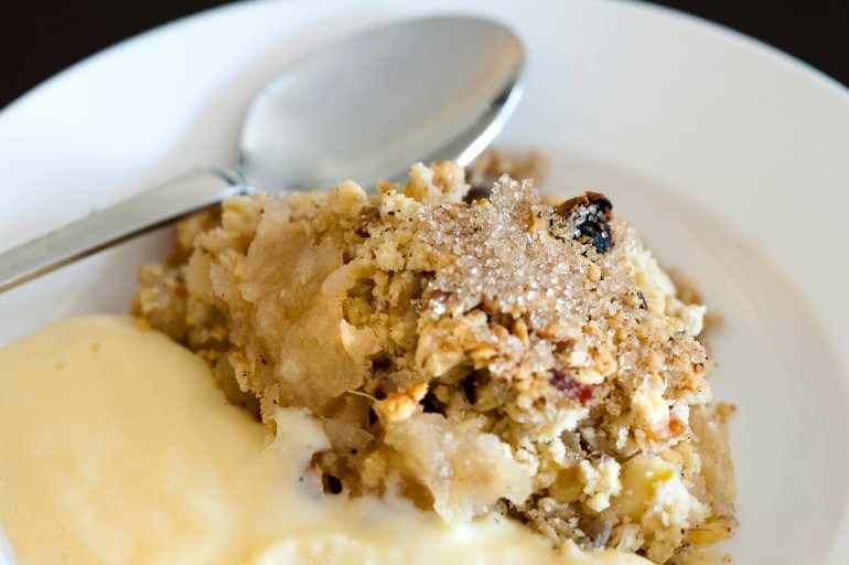 Serving of spicy apple crumble topped with raisins, sugar and cinnamon and served with custard