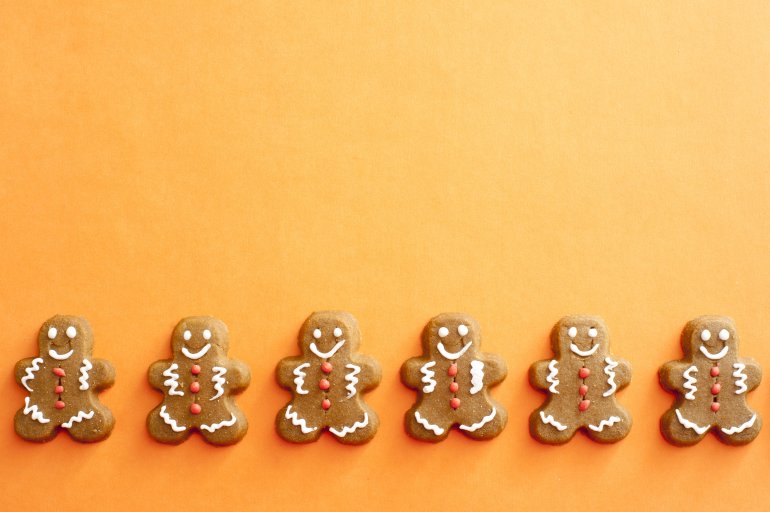 Row of six gingerbread men decorated with white and orange icing details under section of copy space