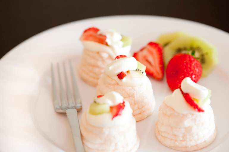 Delicious individual strawberry pavlovas with crispy meringue and fresh fruit served with a fork in a dessert bowl