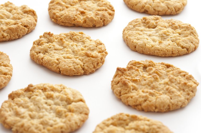 Top down view on cropped white surface with evenly spaced freshly baked round crunchy oat biscuit cookies