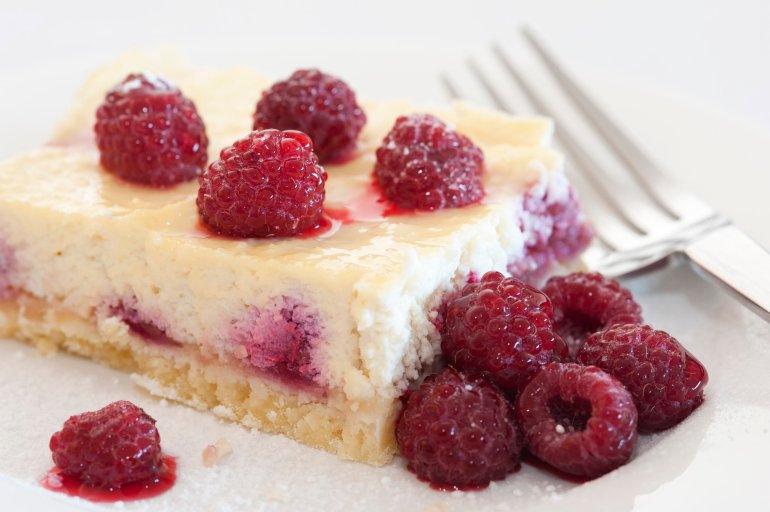 Raspberries on a slice of freshly baked ricotta cheesecake, close up view with a fork