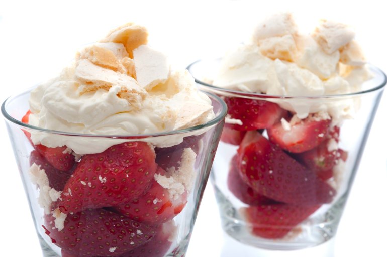 Fresh halved strawberries and whipped cream dessert served in tall glasses, close up view on a white background