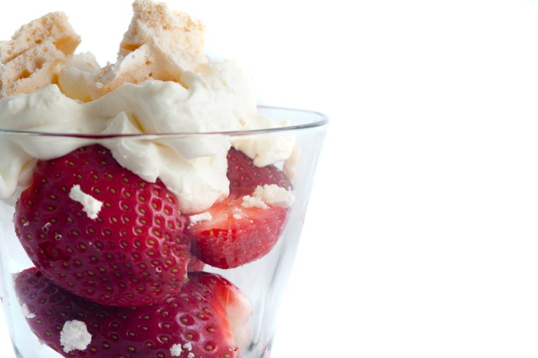 Close up view of a tall glass of delicious strawberries and whipped cream dessert on a white background with copyspace