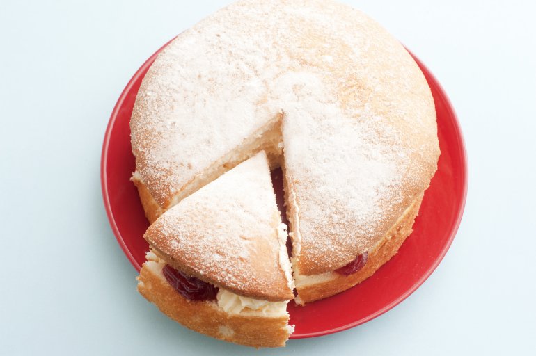 Classic homemade Victoria sandwich or round sponge cake powdered with vanilla sugar on a red plate, close-up with copy space from above