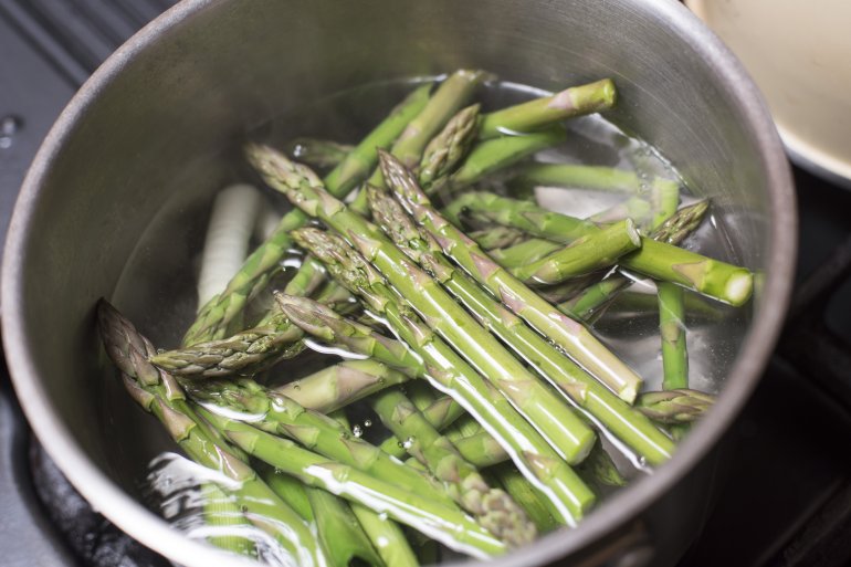 Fresh green asparagus spears boiling in a stainless steel saucepan on a gas hob