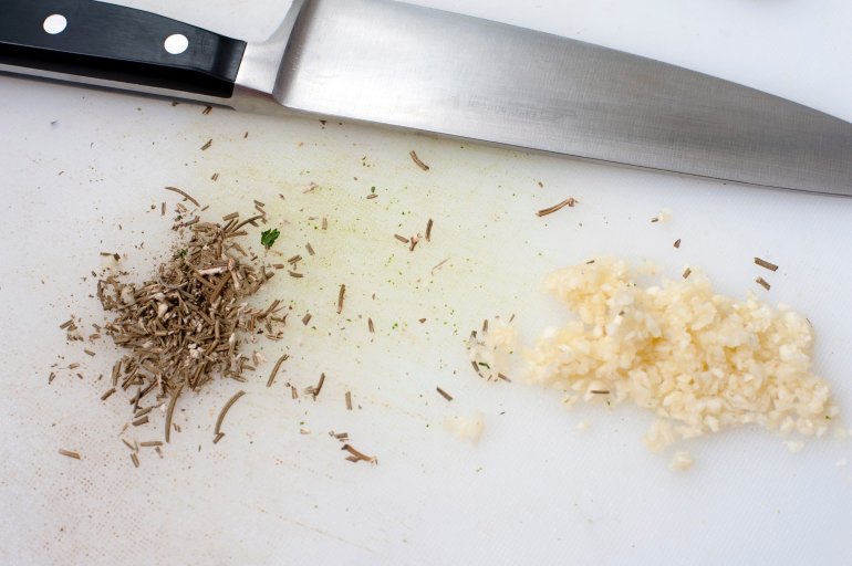 Finely chopped fresh garlic and herbs on a kitchen chopping board with a chefs knife for use in a cooking recipe as a seaoning and aromatic flavouring
