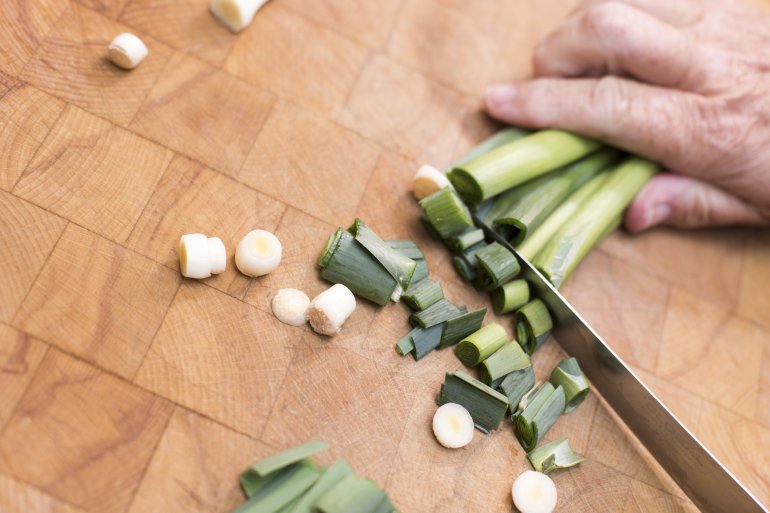 Man chopping fresh leeks for dinner with a large kitchen knife on a marble counter, with copy space