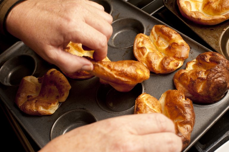 Close up on the hands of a male chef removing cooked individual golden Yorkshire puddings from a baking tray fresh from the oven
