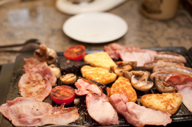 Cooking a hearty English breakfast on a griddle with tomato, bacon, French toast and sausages