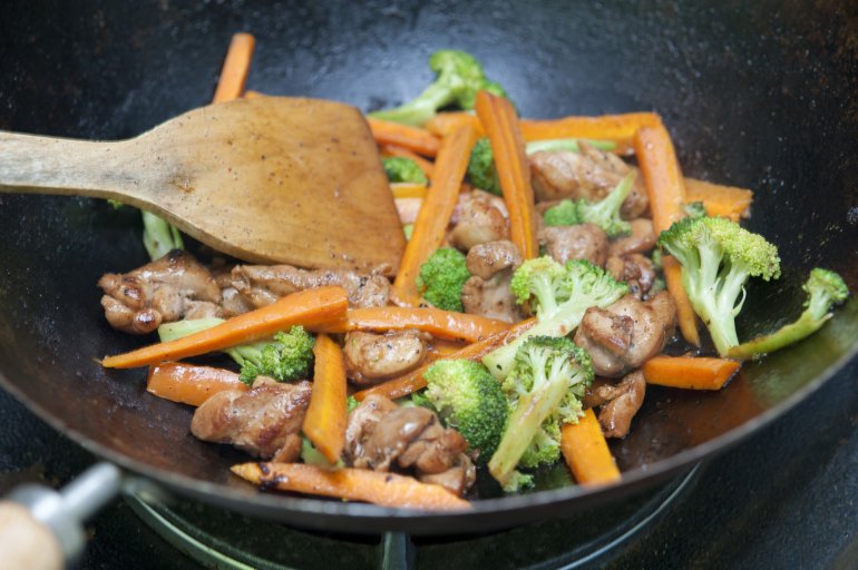 Cooking tasty Asian stir fry with diced fresh vegetables and meat in a wok using a wooden spatula
