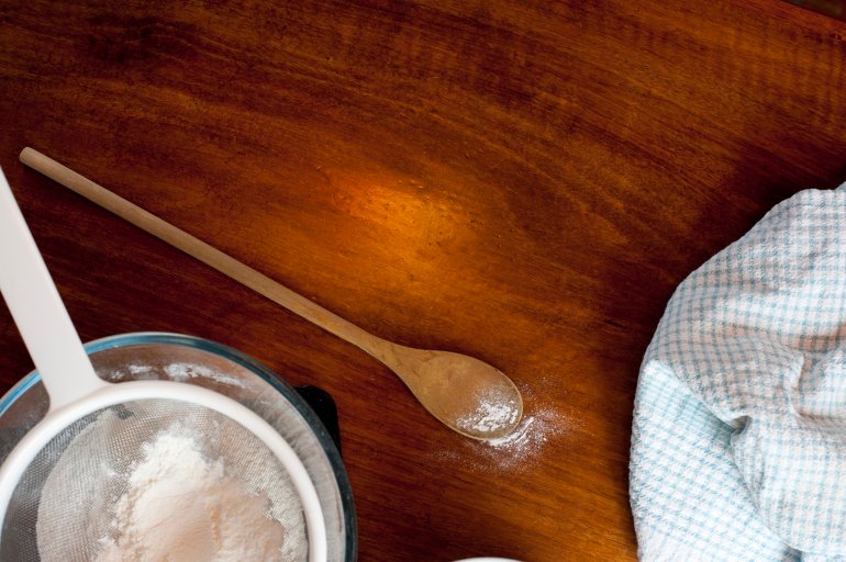 Overhead view of white cake flour in a sieve with a baking spoon on a wooden table with copyspace