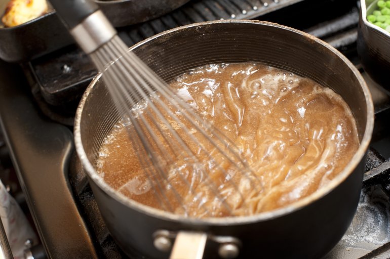 Gravy boiling in a saucepan over a gas hob with a metal manual whisk to prevent lumps on thickening