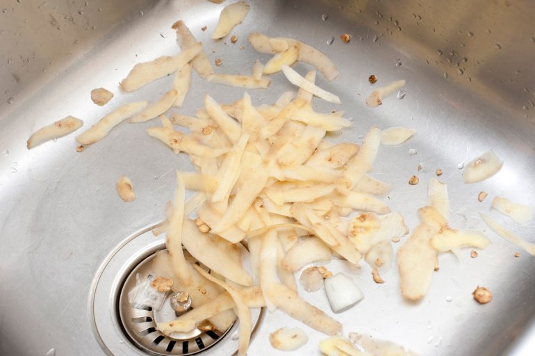 Potato peels lying in a stainless steel kitchen sink waiting to be discarded after preparing the vegetables for cooking