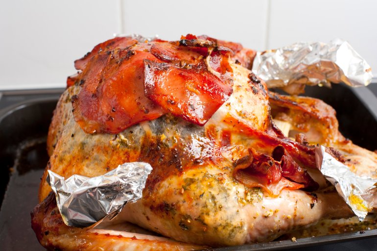 Delicious golden roast festive turkey with garnish and marinade in a roasting or grill pan ready for Thanksgiving or Christmas celebrations