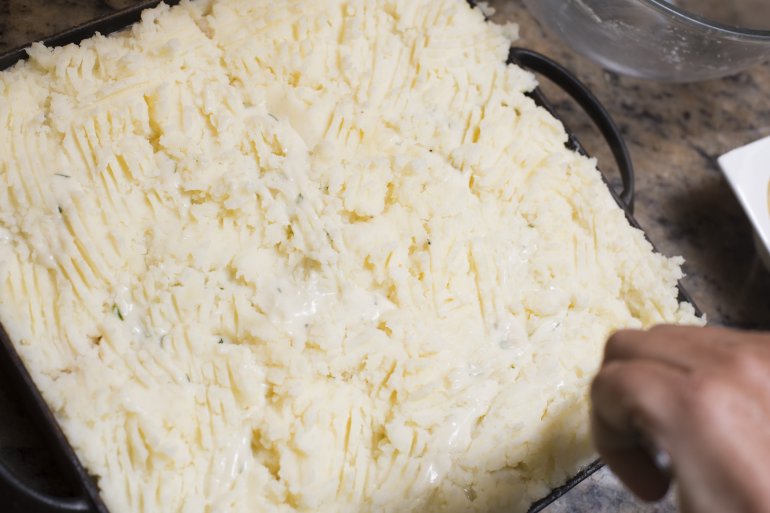Cook topping the cottage pie with mashed potato before placing it in the oven to brown before serving, close up high angle view