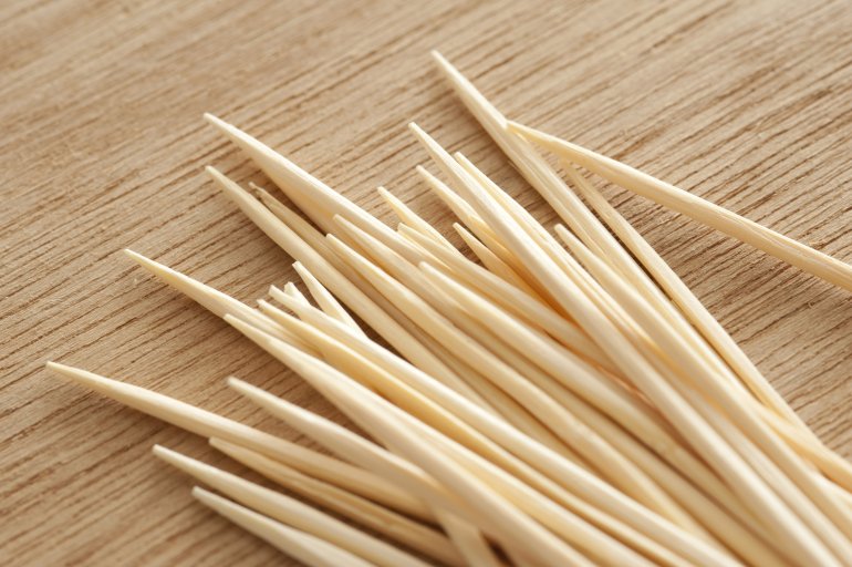 Pile of wooden toothpicks or cocktail sticks in the corner on a wood table for preparing snacks and appetizers in a close up view