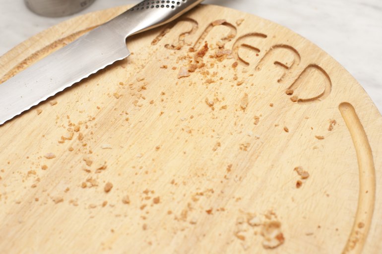 Wooden bread board and knife with crumbs Circular wooden bread board with inscribed text and a stainless steel knife with scattered crumbs on its surface after the bread is removed