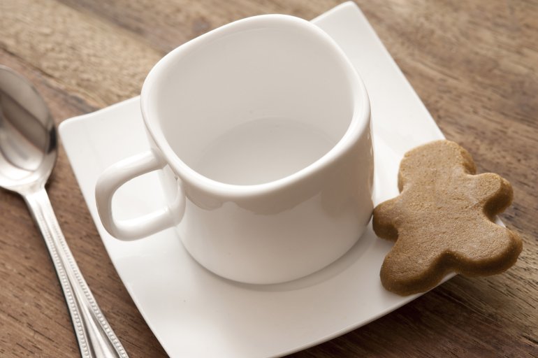 Clean empty white demitasse cup with square saucer for espresso coffee and a gingerbread cookie on a wooden table