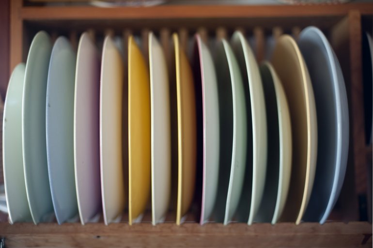 Selection of dinner plates in a wooden rack Selection of clean colourful dinner plates in a wooden rack mounted on a kitchen wall ready to be used to serve the food