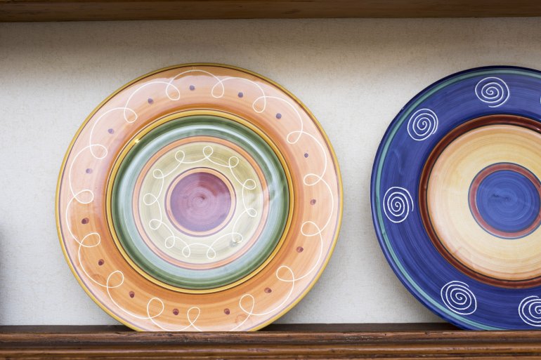 Colorful patterned ceramic dinner plates Colorful patterned ceramic dinner plates on display on a wall mounted wooden shelf in a close up view