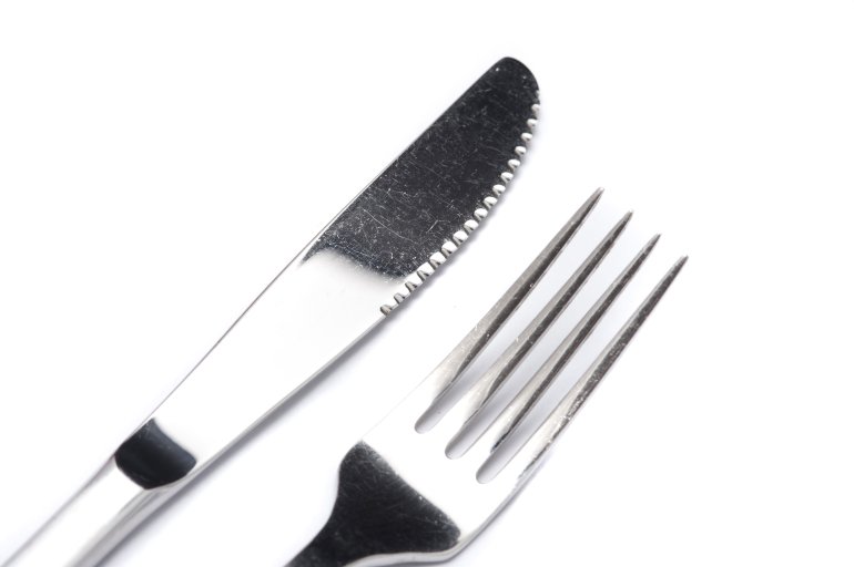 Clean silver knife and fork close up on white arranged diagonally from the corner viewed from above in a catering concept