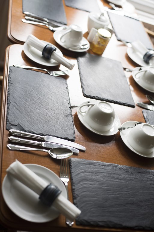 Laid wooden dining table in a restaurant with cutlery, crockery and linen in a close up cropped view of a single place setting