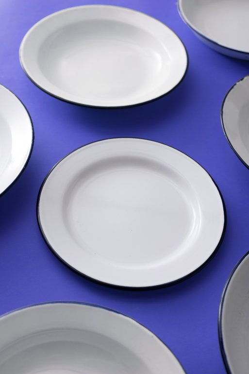 Clean empty white enamelled metal kitchen plates on a bright blue surface scattered randomly viewed high angle