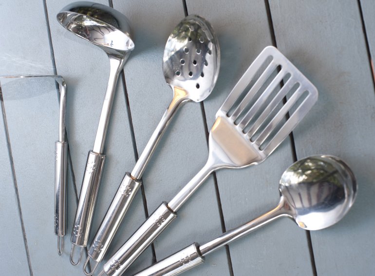Set of silver metal kitchen utensils for cooking fanned out on a rustic grey slatted wood table in a high angle view