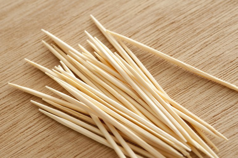 Stack of clean wooden toothpicks or cocktail sticks on a wood table in a close up view ready to use in preparing snacks or for dental hygiene at a dinner table