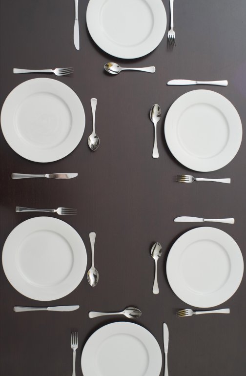 Dark table set for six people with clean white plates and cutlery viewed from above