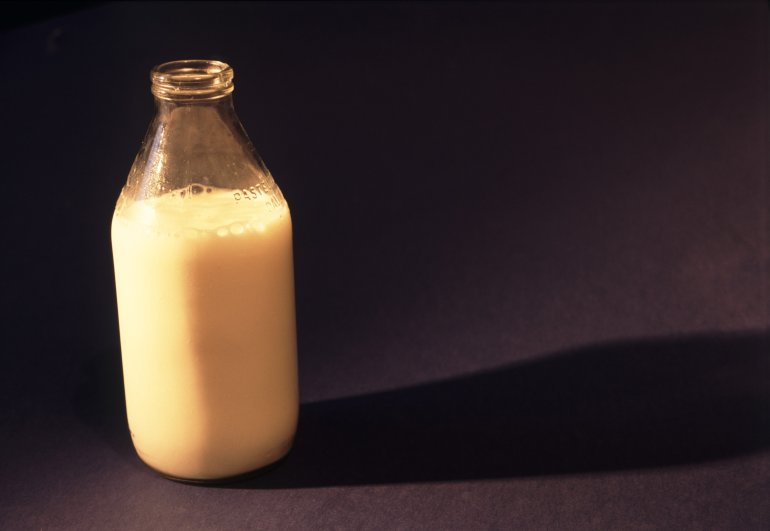 Traditional clear glass bottle of delicious fresh creamy cows milk on a black background with copyspace