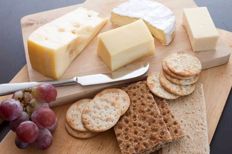 Assorted cheese platter served on a buffet as an appetizer with crackers, water biscuits and a small bunch of fresh red grapes