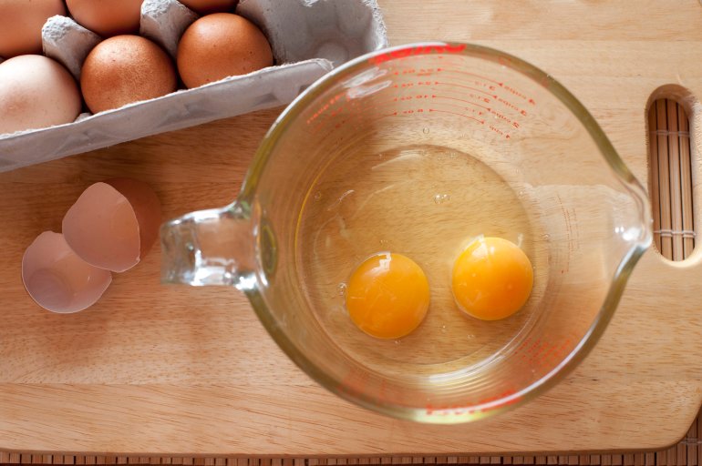 Overhead view of two cracked eggs with rich yellow yolks in a measuring jug on a kitchen counter for use as a baking ingredient